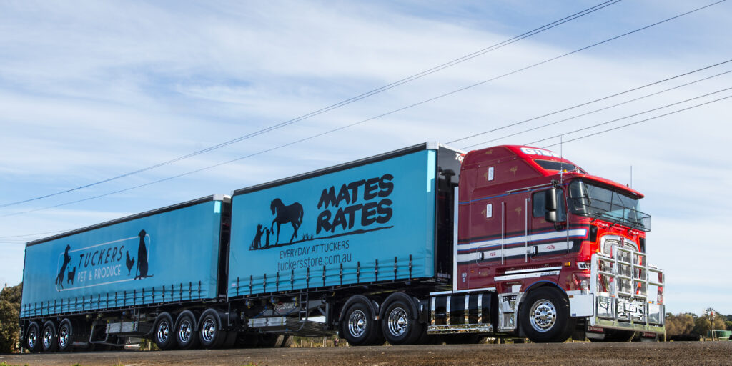 Red Gibbtrans Kenworth K200 Big Cab hauling blue B-double curtain-side trailers