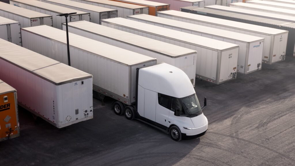 White Tesla Semi with a box trailer in a freight yard.