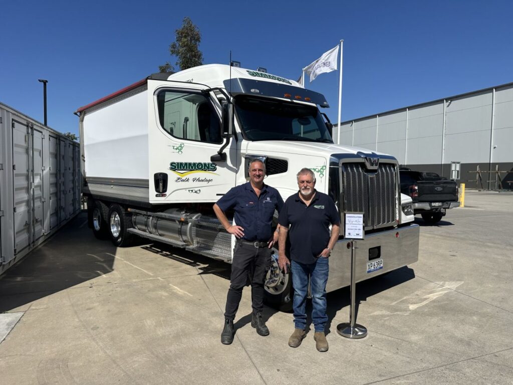 White Simmons Bulk Haulage Western Star 48X truck at Trucksmart handover, with two people standing beside the vehicle.